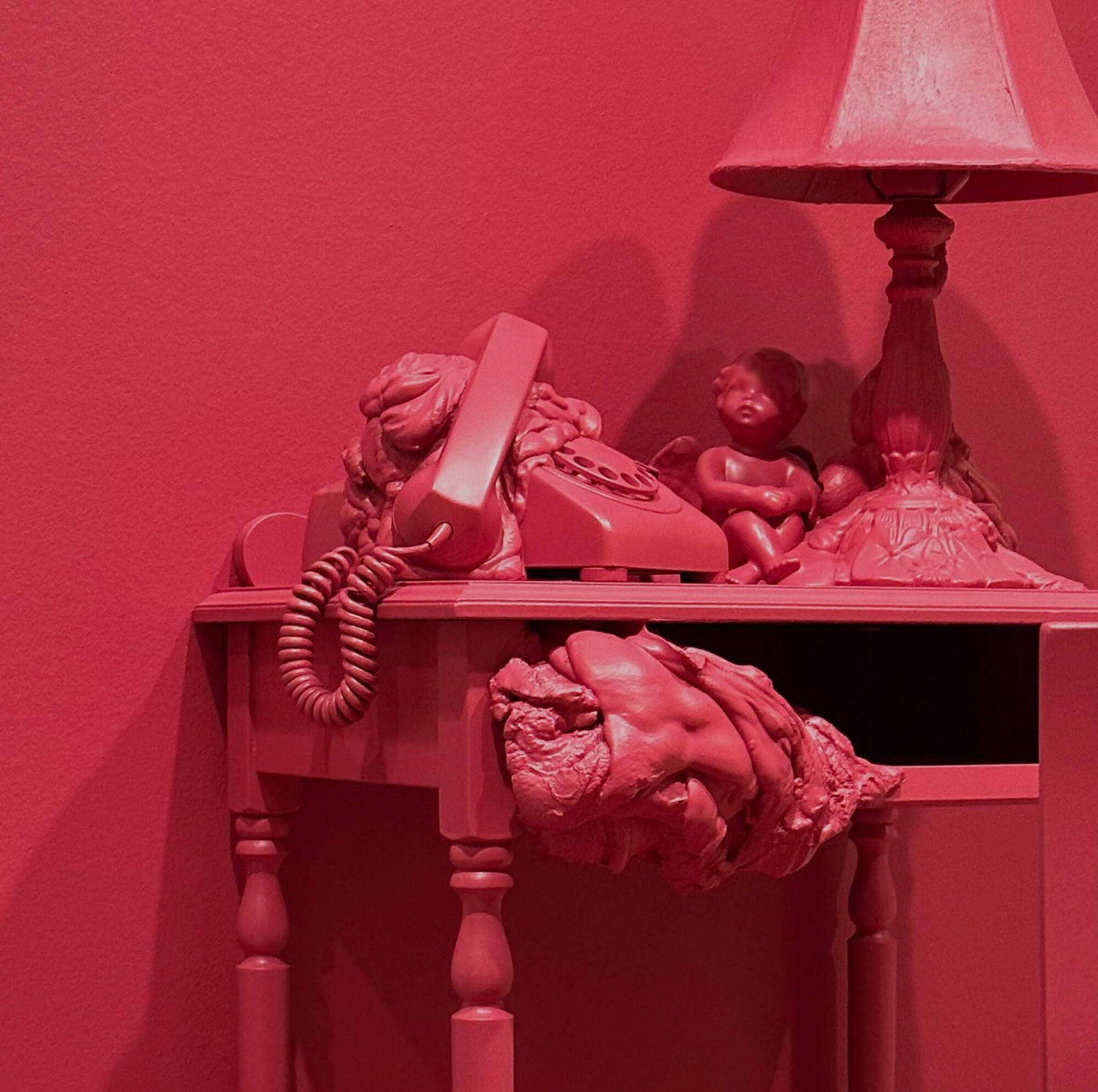 A photograph of a side table with a telephone, lamp, and organic shapes all painted bright pink